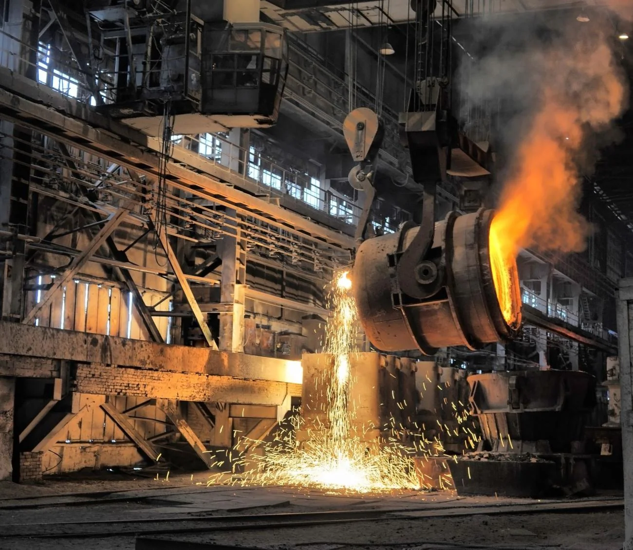 Glowing molten hot metal pouring from a ladle in a steel plant cast house